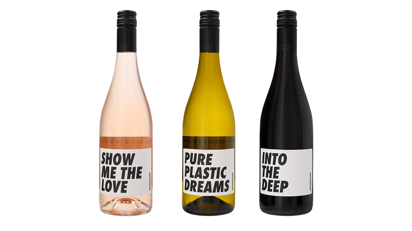 Drie flessen wijn met zwarte doppen en etiketten: Show Me The Love Rosé, Pure Plastic Dreams Chardonnay, Into The Deep Merlot.